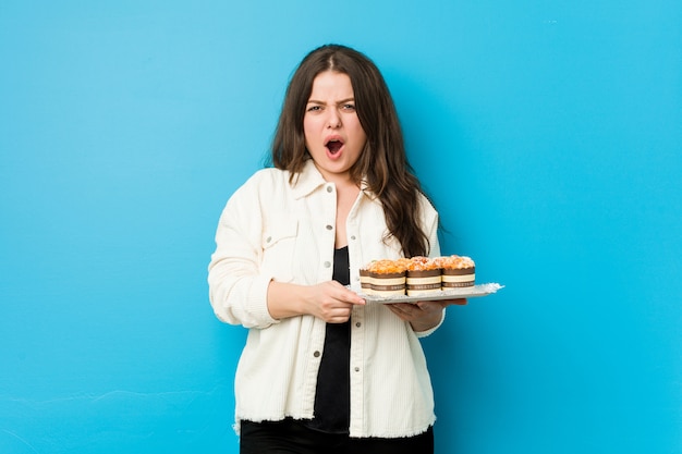 Giovane donna curvy in possesso di un cupcakes urlando molto arrabbiato e aggressivo