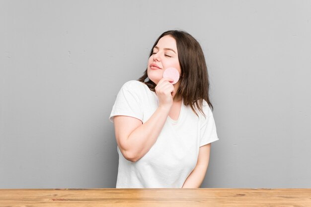 Young curvy woman holding a facial disk isolated on a grey wall