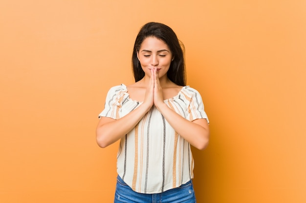 Young curvy woman holding hands in pray near mouth, feels confident.