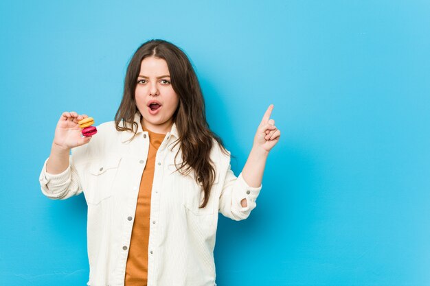 Young curvy woman holding macaroons pointing to the side