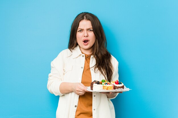 Young curvy woman holding a sweet cakes screaming very angry and aggressive.