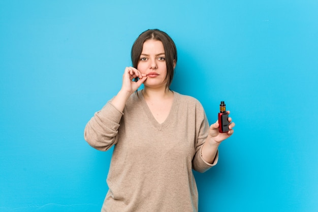 Young curvy woman holding a vaporizer with fingers on lips keeping a secret.