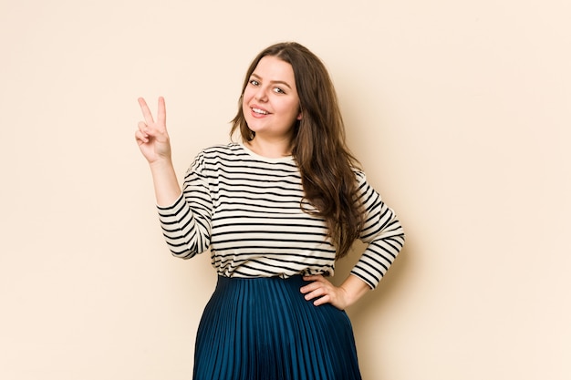 Young curvy woman joyful and carefree showing a peace symbol with fingers.