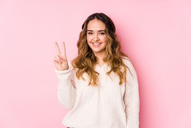 Young curvy woman posing in a pink wall isolated showing number two with fingers.