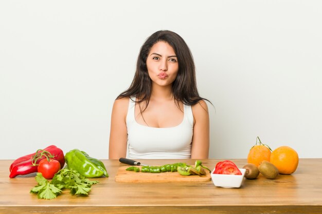 健康的な食事を準備する若い曲線の女性は、頬を吹く、疲れた表情をしています。表情のコンセプト。