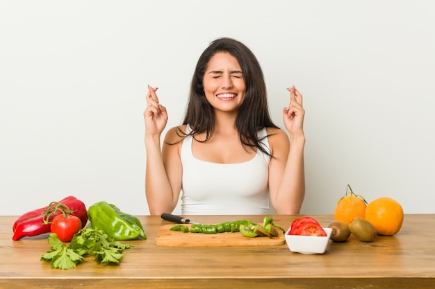 Young curvy woman preparing a healthy meal crossing fingers for having luck