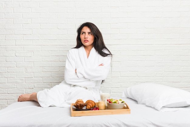 Young curvy woman taking a breakfast on the bed tired of a repetitive task.