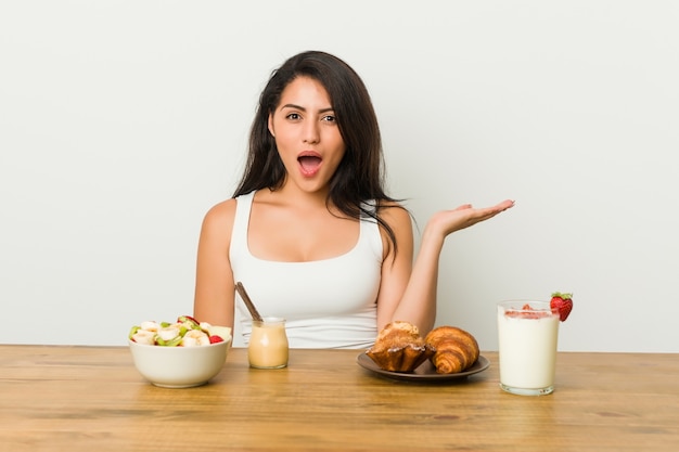 Young curvy woman taking a breakfast impressed holding  on palm.