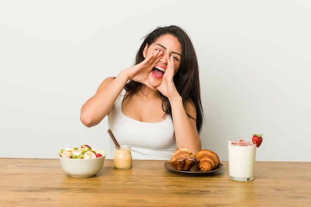 Young curvy woman taking a breakfast shouting excited to front.