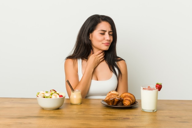 Young curvy woman taking a breakfast suffers pain in throat due a virus or infection.