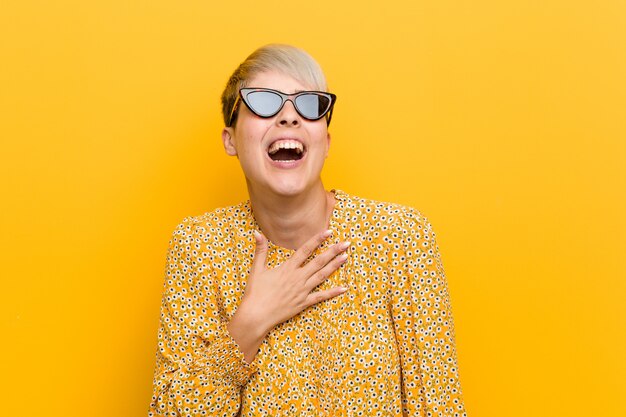 Young curvy woman wearing a floral summer clothes laughs out loudly keeping hand on chest.