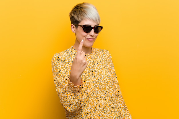 Young curvy woman wearing a floral summer clothes pointing with finger at you as if inviting come closer.