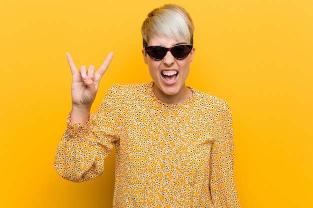 Young curvy woman wearing a floral summer clothes showing a horns gesture as a revolution concept.