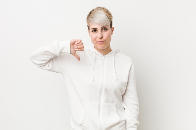 Young curvy woman wearing a white hoodie showing a dislike gesture, thumbs down. Disagreement concept.