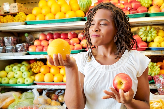 Young customer holding fruits in her hands and choosing the ripe ones during shopping in the store