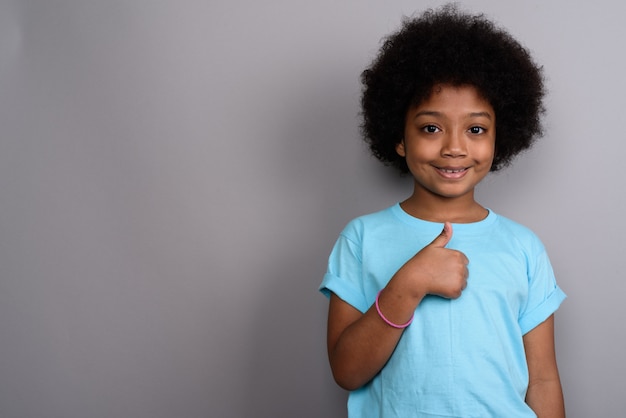 Young cute African girl against gray wall