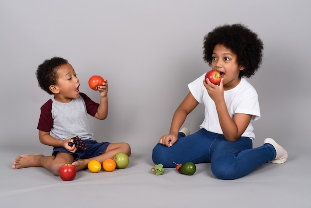 Young cute African siblings together against gray wall