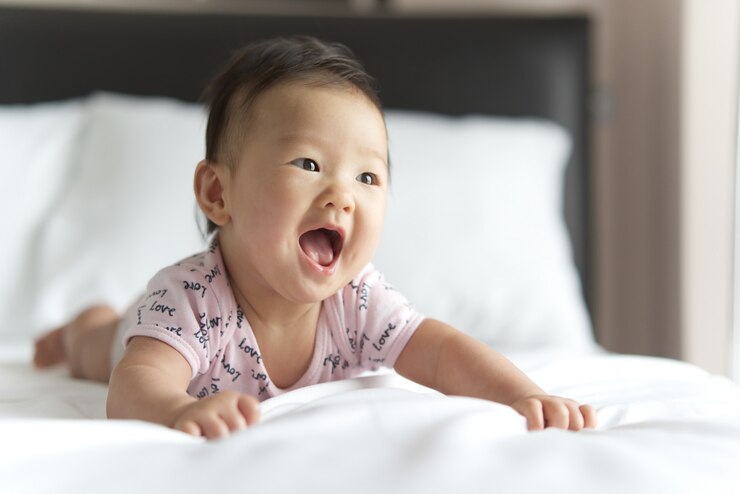 若いかわいいアジアの赤ちゃんが寝室のベッドの上でクロールします。その赤ちゃんは微笑み、まっすぐに見えています。