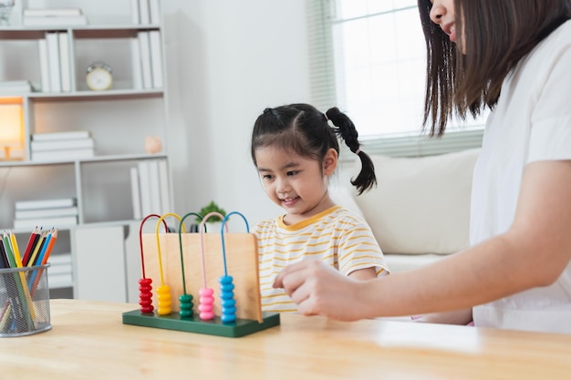 Young cute Asian girl and her parent mother mom is learning the abacus with colored beads to learn how to count sofa in the living room at home Child baby girl development studing concept