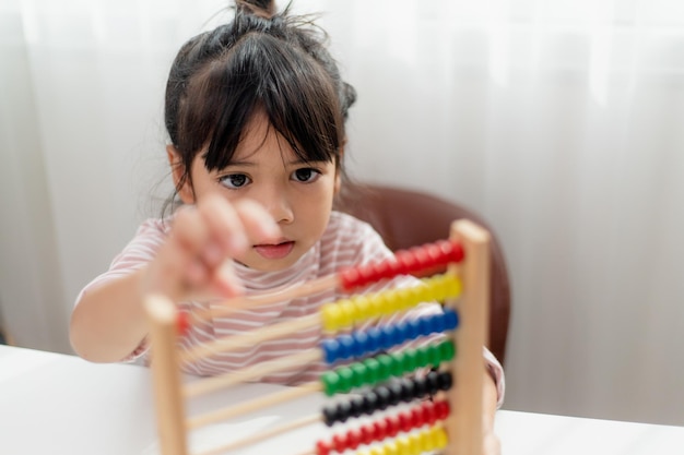 A young cute Asian girl is using the abacus with colored beads to learn how to count at home