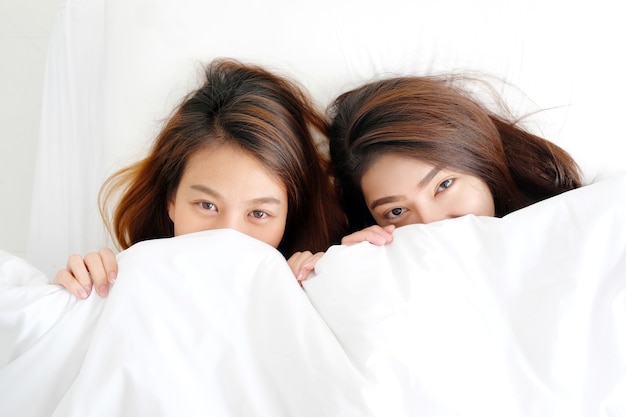 Giovani lesbiche asiatiche sveglie che si trovano insieme sul letto bianco di mattina