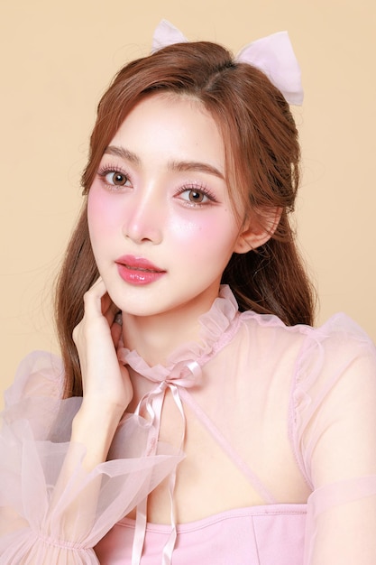 Young cute Asian woman in a pink elegant dress Korean style makeup moisturized smooth perfect skin on a beige background Facial treatment Cosmetology plastic surgery