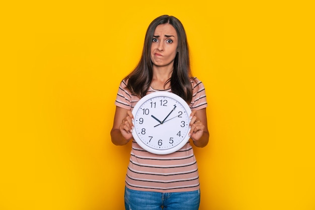 Young cute attractive woman with big white clock in hands shows this on the camera