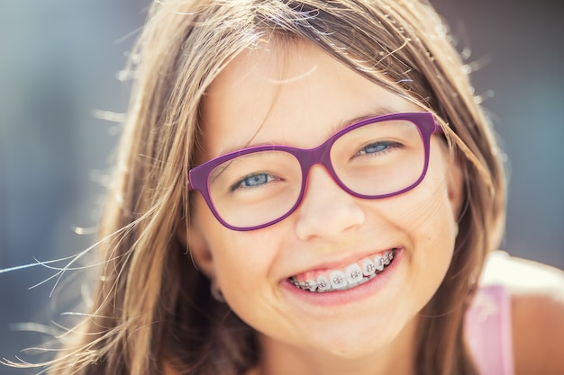 Giovane ragazza bionda caucasica carina che indossa bretelle e occhiali per i denti