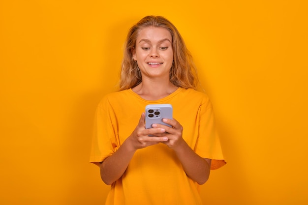 Young cute cheerful caucasian woman blogger holding mobile phone typing new post