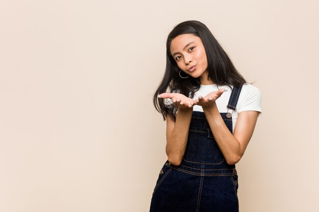 Young cute chinese teenager  woman  against a pink wall folding lips and holding palms to send air kiss.