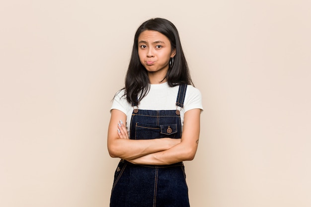 Giovane adolescente cinese carino giovane donna bionda che indossa un cappotto contro un muro rosa soffia le guance, ha un'espressione stanca. concetto di espressione facciale.