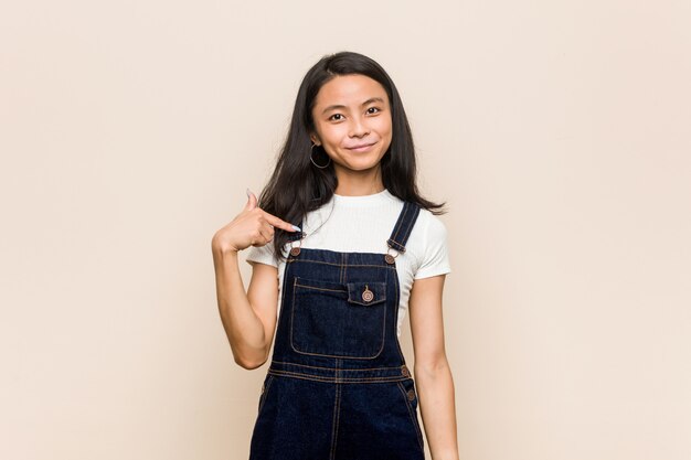 Young cute chinese teenager Young blonde woman wearing a coat against a pink wall person pointing by hand to a shirt copy space, proud and confident