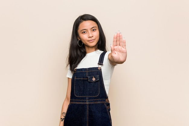 Young cute chinese teenager Young blonde woman wearing a coat against a pink wall standing with outstretched hand showing stop sign, preventing you.