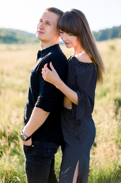 Молодая милая влюбленная пара в стильной черной одежде позирует на летнем лугу