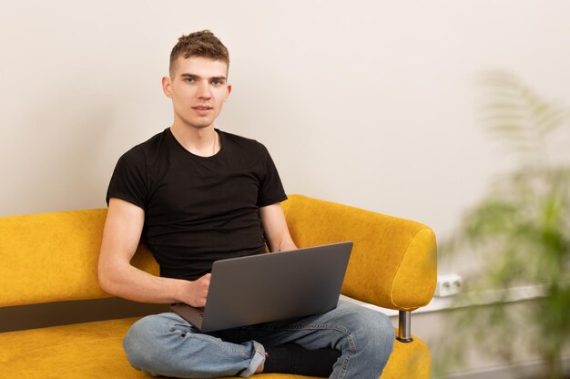 Young cute gamer sitting on sofa and playing on laptop