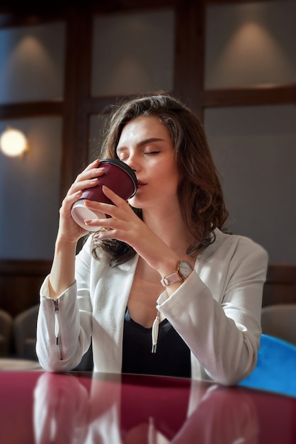 Young cute girl drinking coffee in cafe