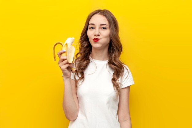 young cute girl eating banana on yellow isolated background woman biting fruit healthy eating