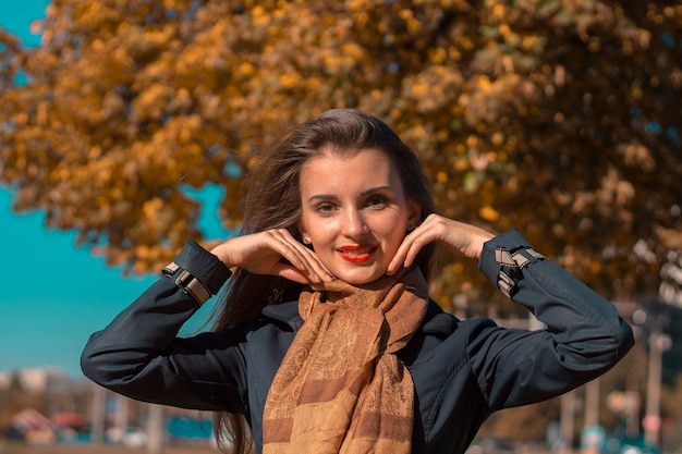 Young cute girl is standing on the street smiles and raised her hands to the face