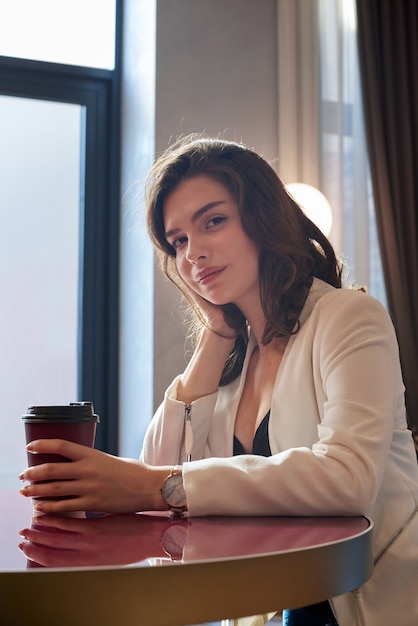 Young cute girl smiling and drinking coffee in a cafe