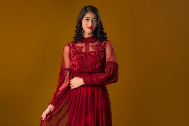 Young cute girl wearing a beautiful red dress posing on brown background