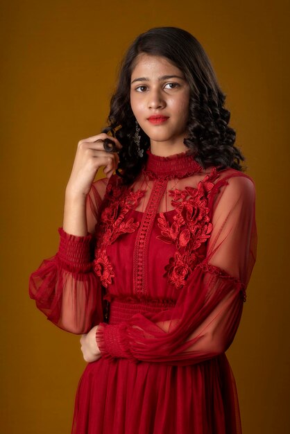 Young cute girl wearing a beautiful red dress posing on brown background