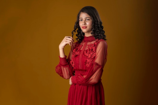 Photo young cute girl wearing a beautiful red dress posing on brown background