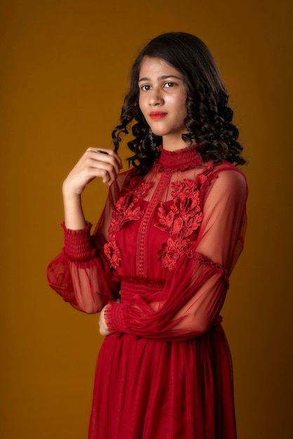 Young cute girl wearing a beautiful red dress posing on brown background