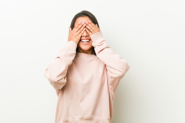 Young cute hispanic teenager woman covers eyes with hands, smiles broadly waiting for a surprise.