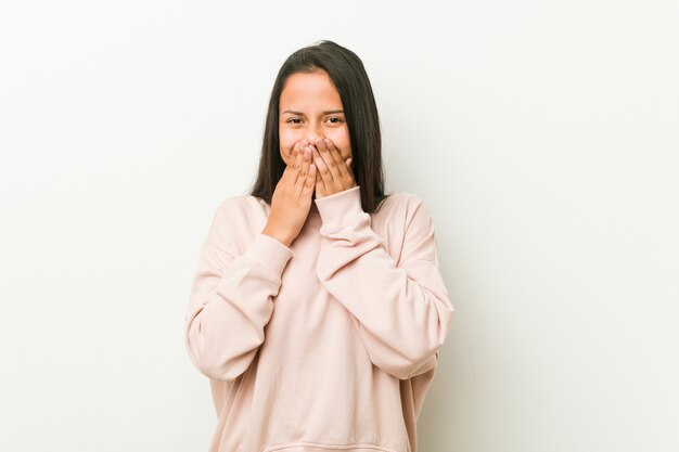 Young cute hispanic teenager woman laughing about something, covering mouth with hands.