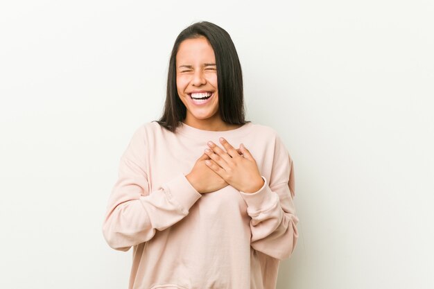 Young cute hispanic teenager woman laughing keeping hands on heart, concept of happiness.