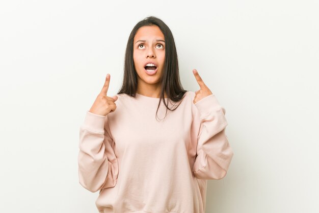 Young cute hispanic teenager woman pointing upside with opened mouth.