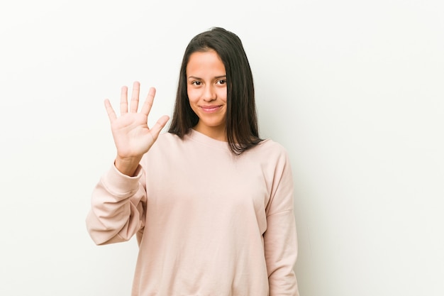 Giovane donna ispanica carina adolescente sorridente allegro che mostra il numero cinque con le dita.