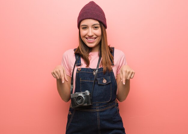 Young cute photographer woman pointing to the bottom with fingers