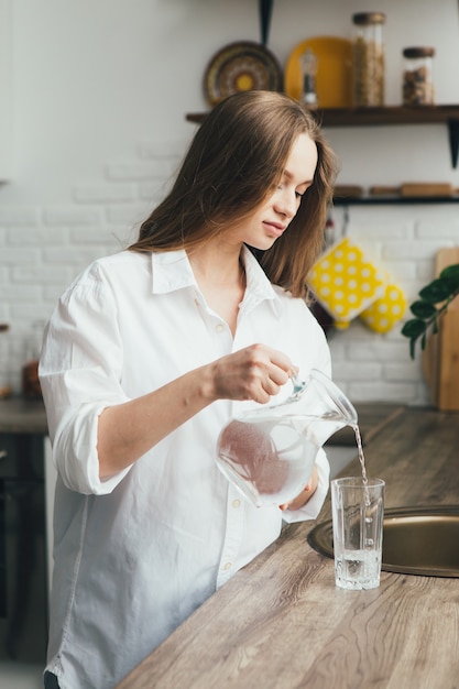 Young cute pregnant girl drinking clean water in the kitchen